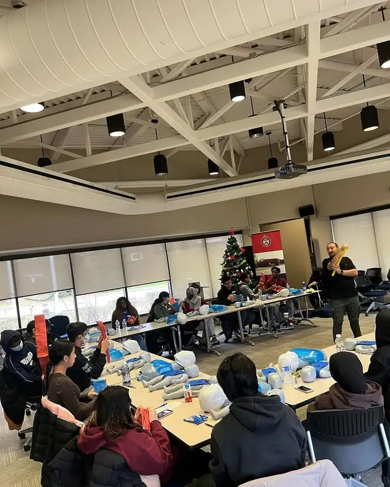 Youth practising on CPR manikins at tables during a training session led by an instructor